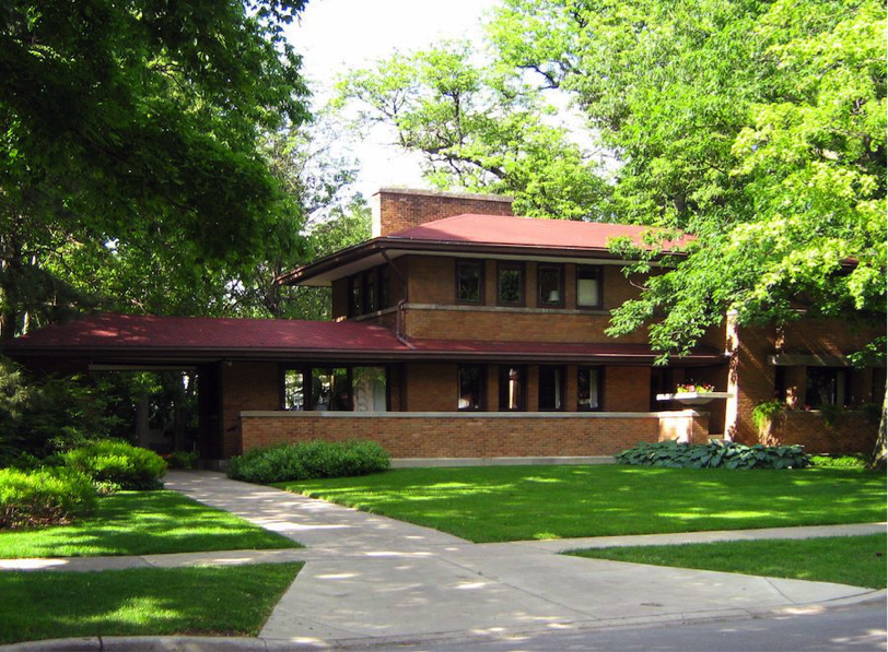 Description: The exterior of the Harry S. Adams house. The facade is red brick. The house is surrounded by trees.